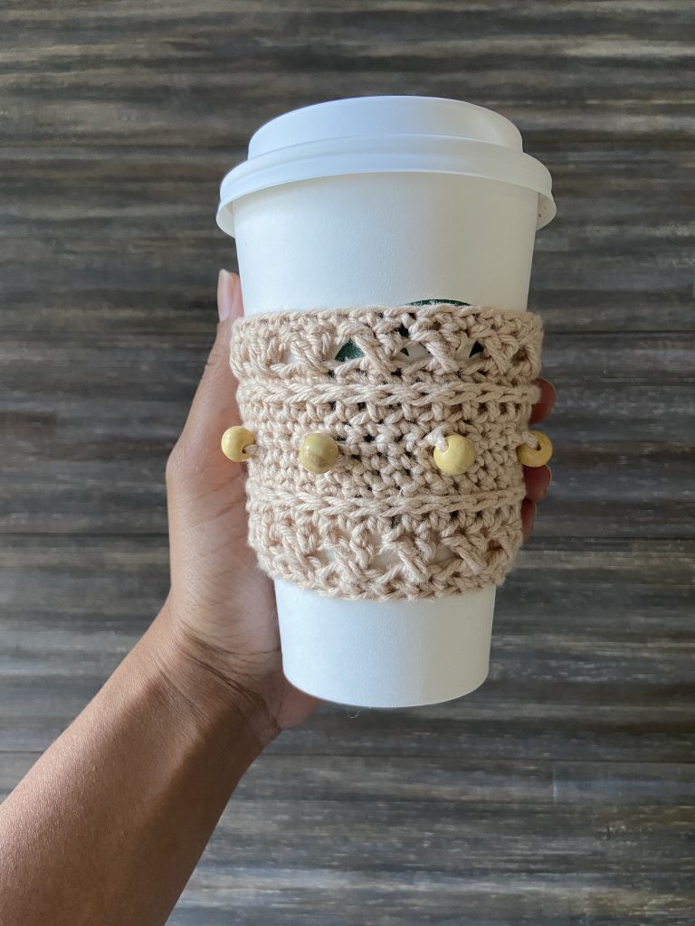 overhead view of hand holding starbucks travel cup with tan beaded cup cozy