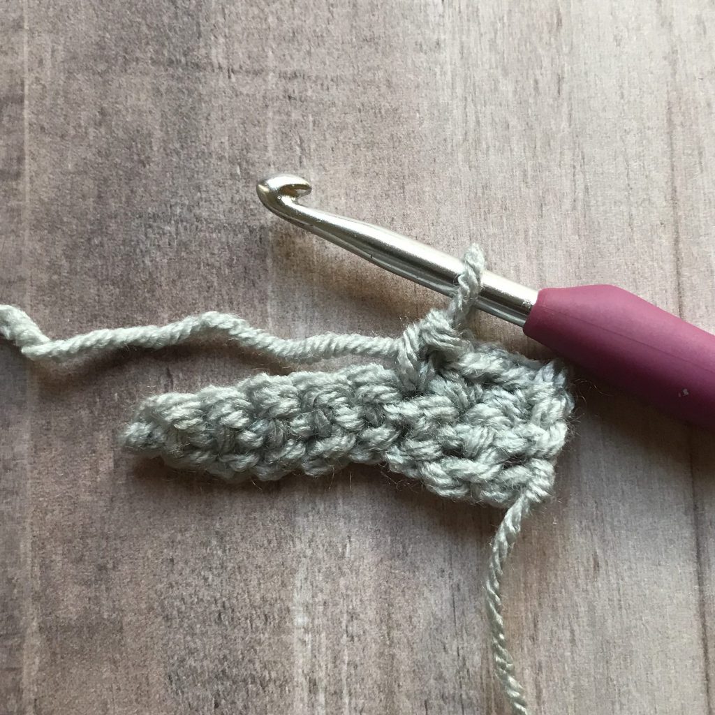 crochet hook pulling up loop in gray crochet fabric