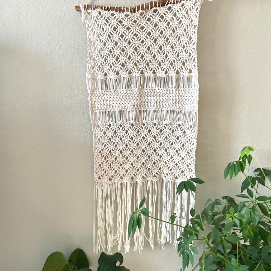 cream crochet wall hanging with plants in foreground