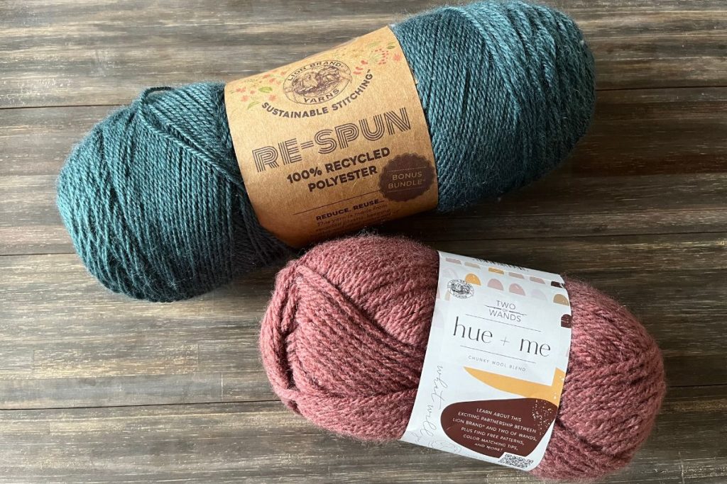 a skein of teal yarn next to a skein of rose yarn on a wood background