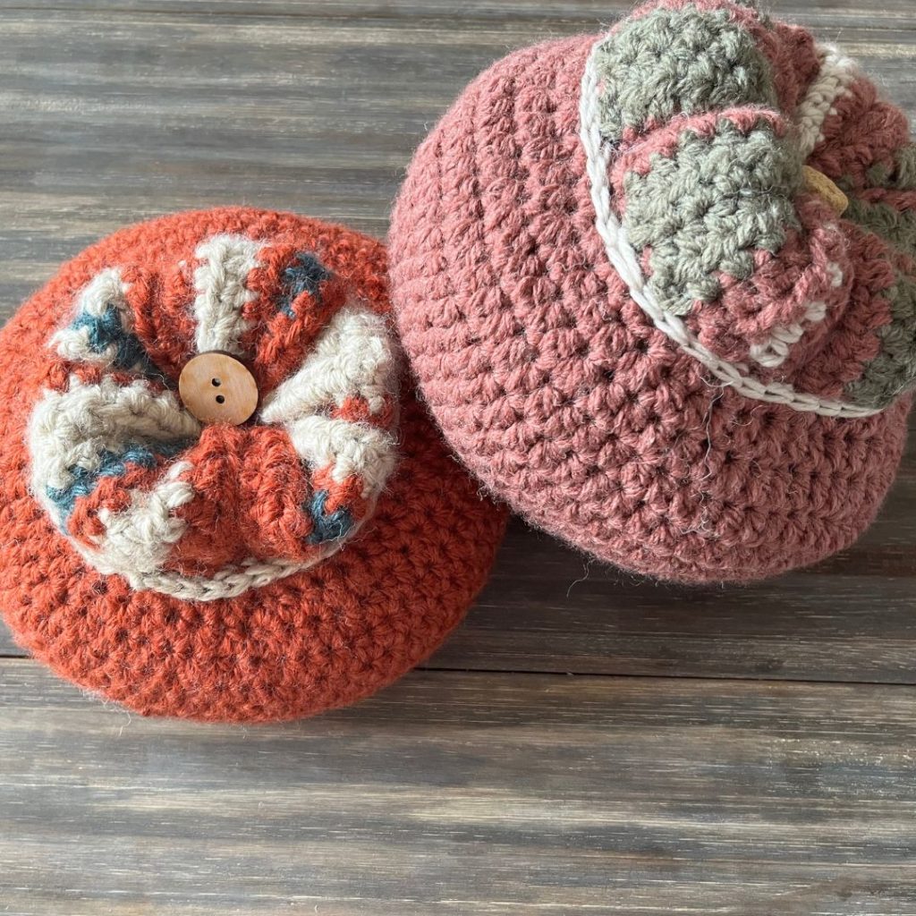 crochet turban squash in light re color leaning on second turban squash in orange red color on wood background 