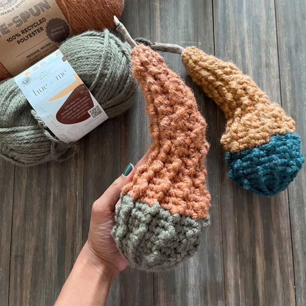 hand holding crochet textured two-tone bottled neck gourd beside second gourd and yarn skeins