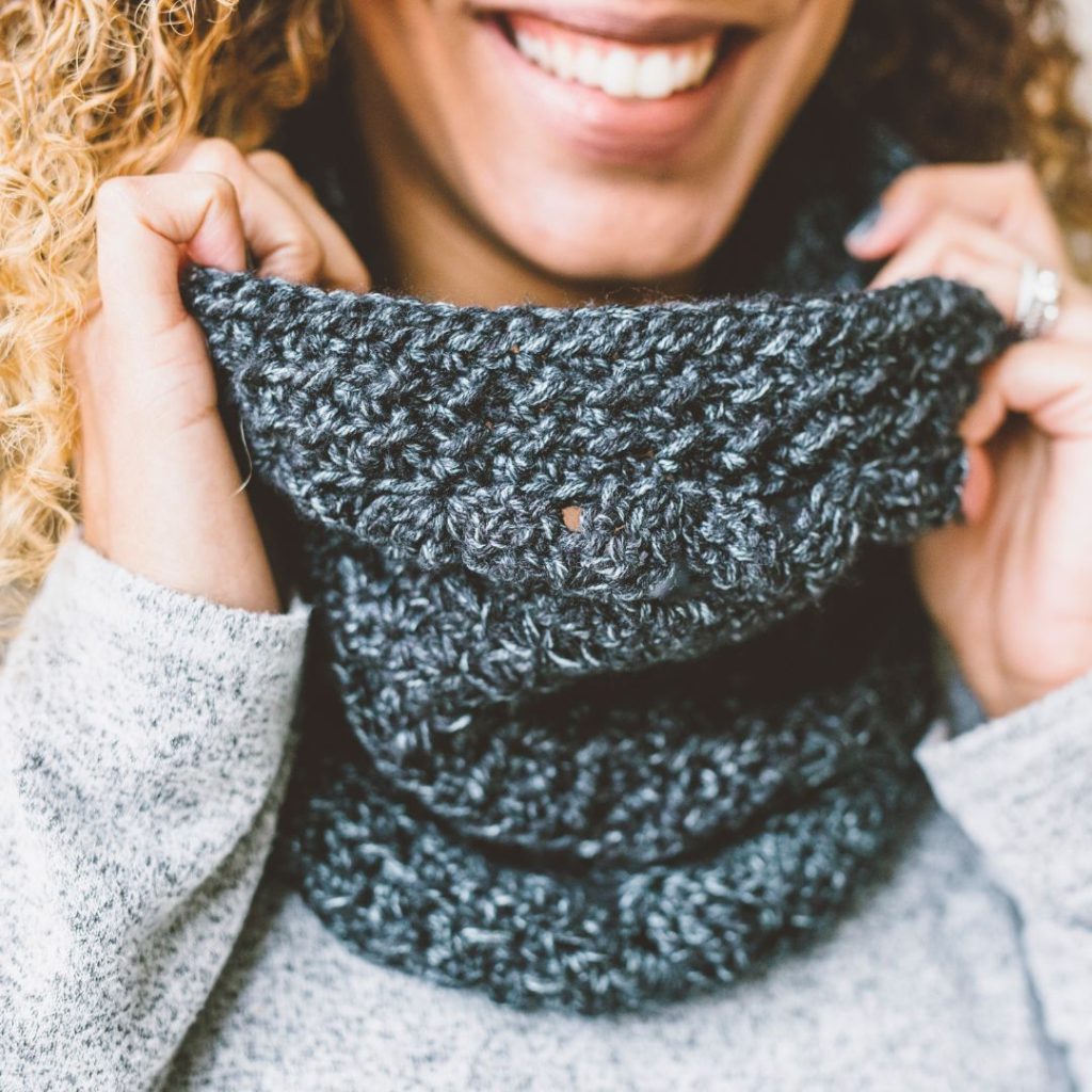 woman wearing charcoal colored crocheted cowl and holding it with two hands to show fabric