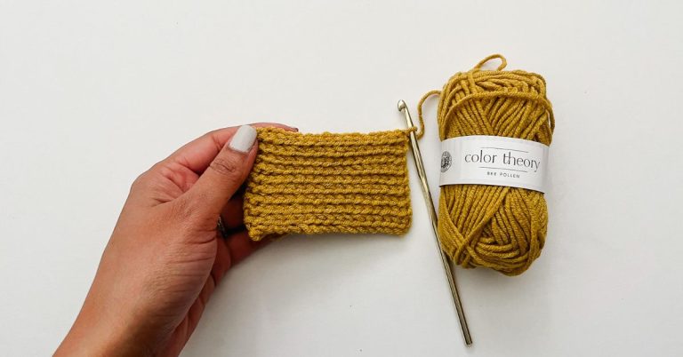 hand holding yellow crochet swatch of slip stitch on white background with gold crochet hook and mini yarn skein