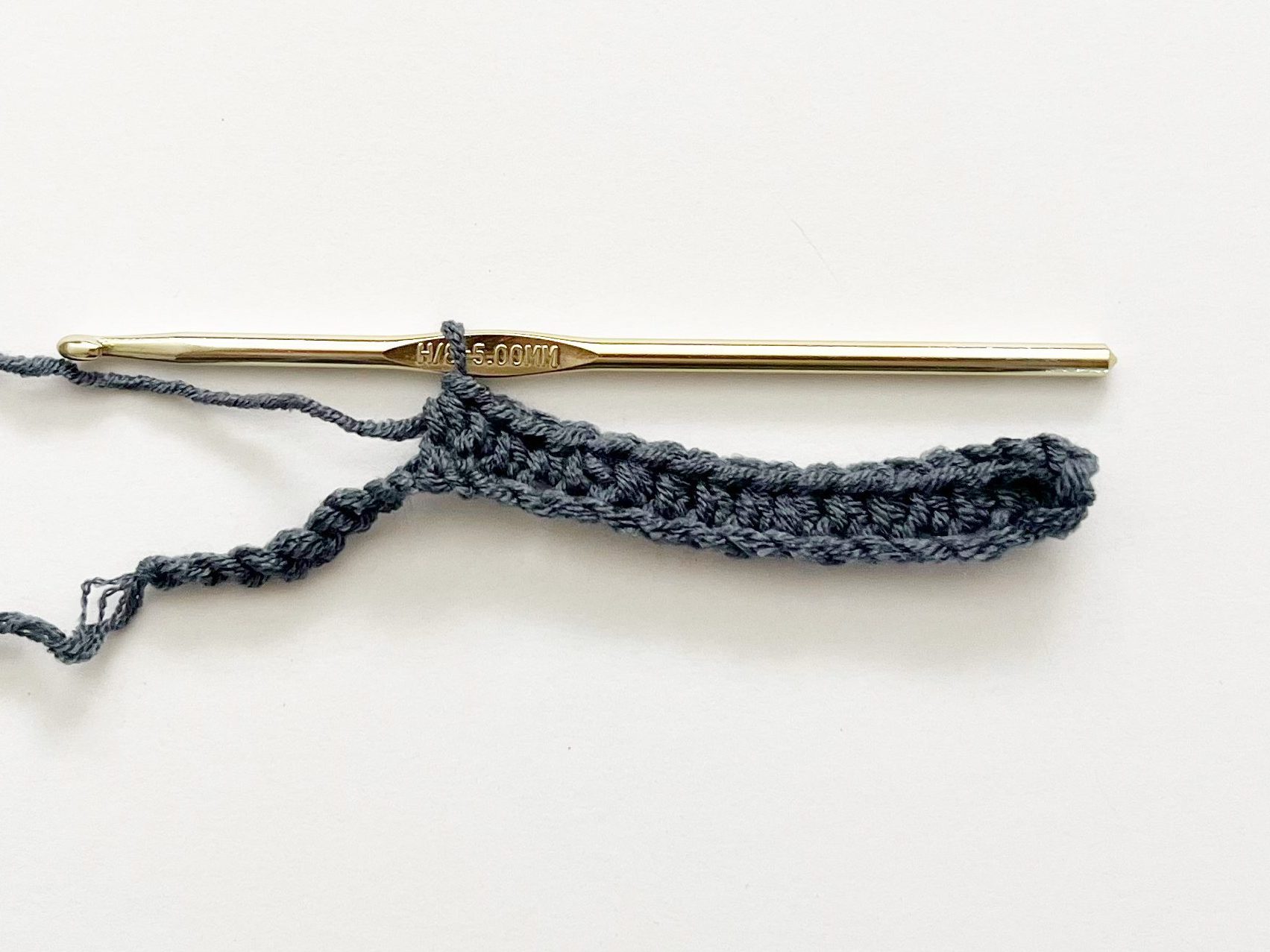 denim blue yarn showing crochet half double crochet stitch with gold hook on white background 