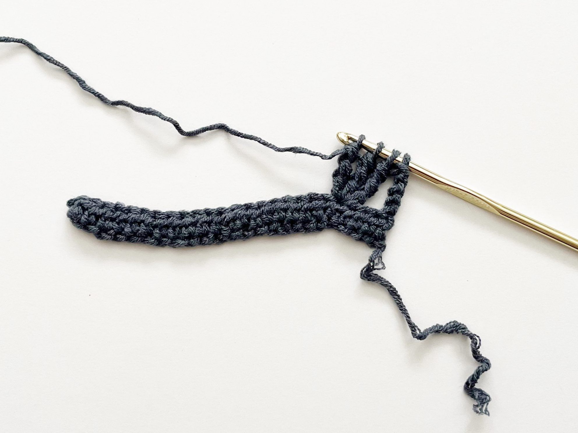 denim blue yarn and gold hook demonstrating double treble crochet stitch