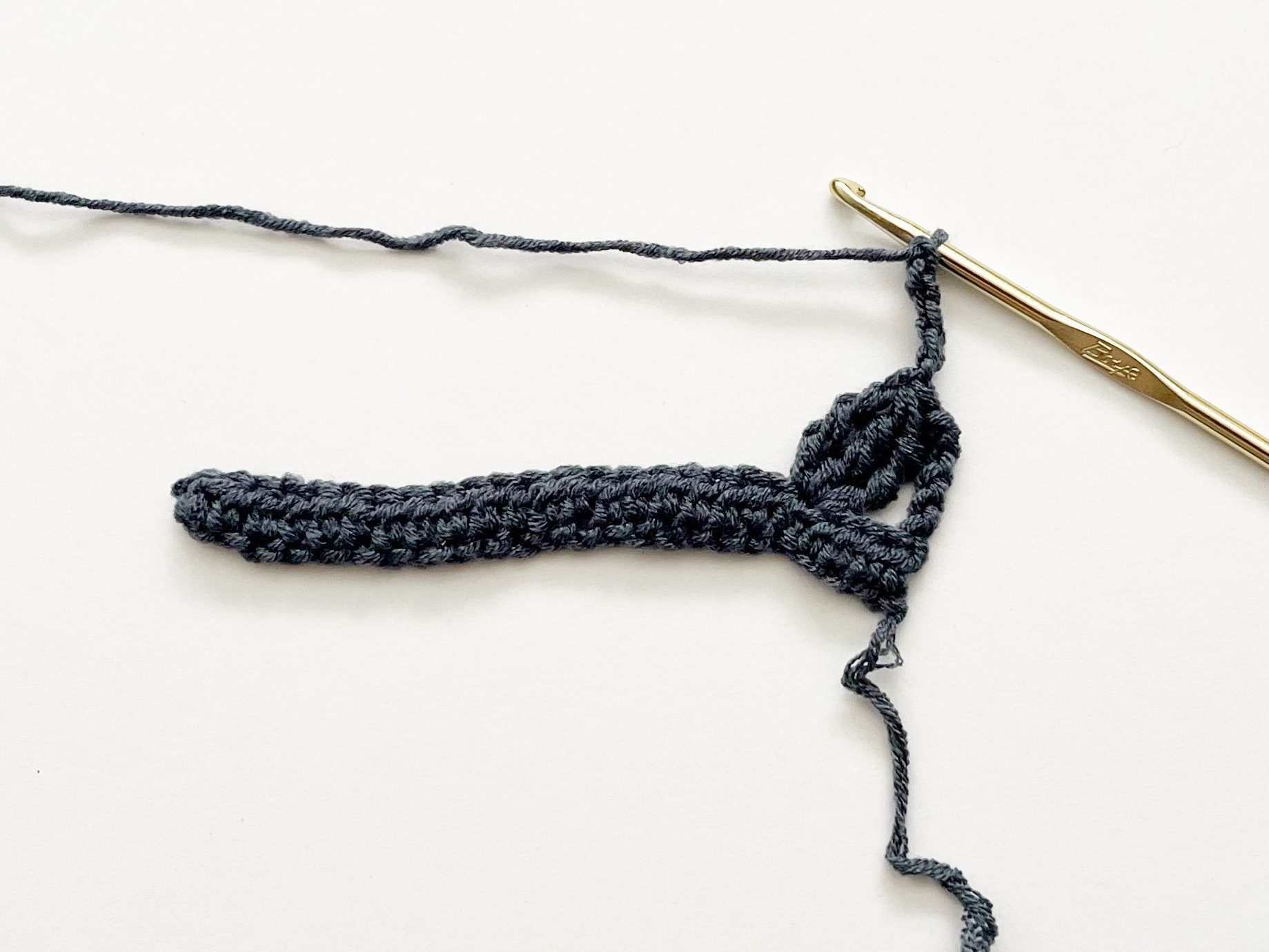denim blue yarn and gold hook demonstrating chain stitches on white background