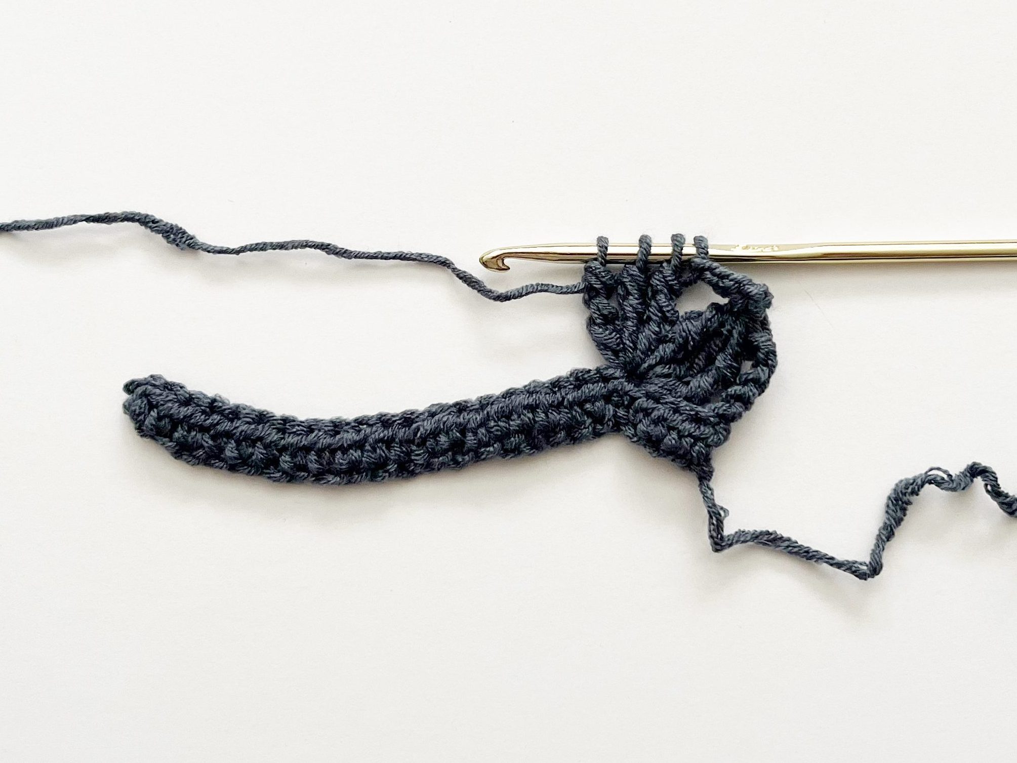 denim blue yarn and gold hook showing double treble crochet group on white background