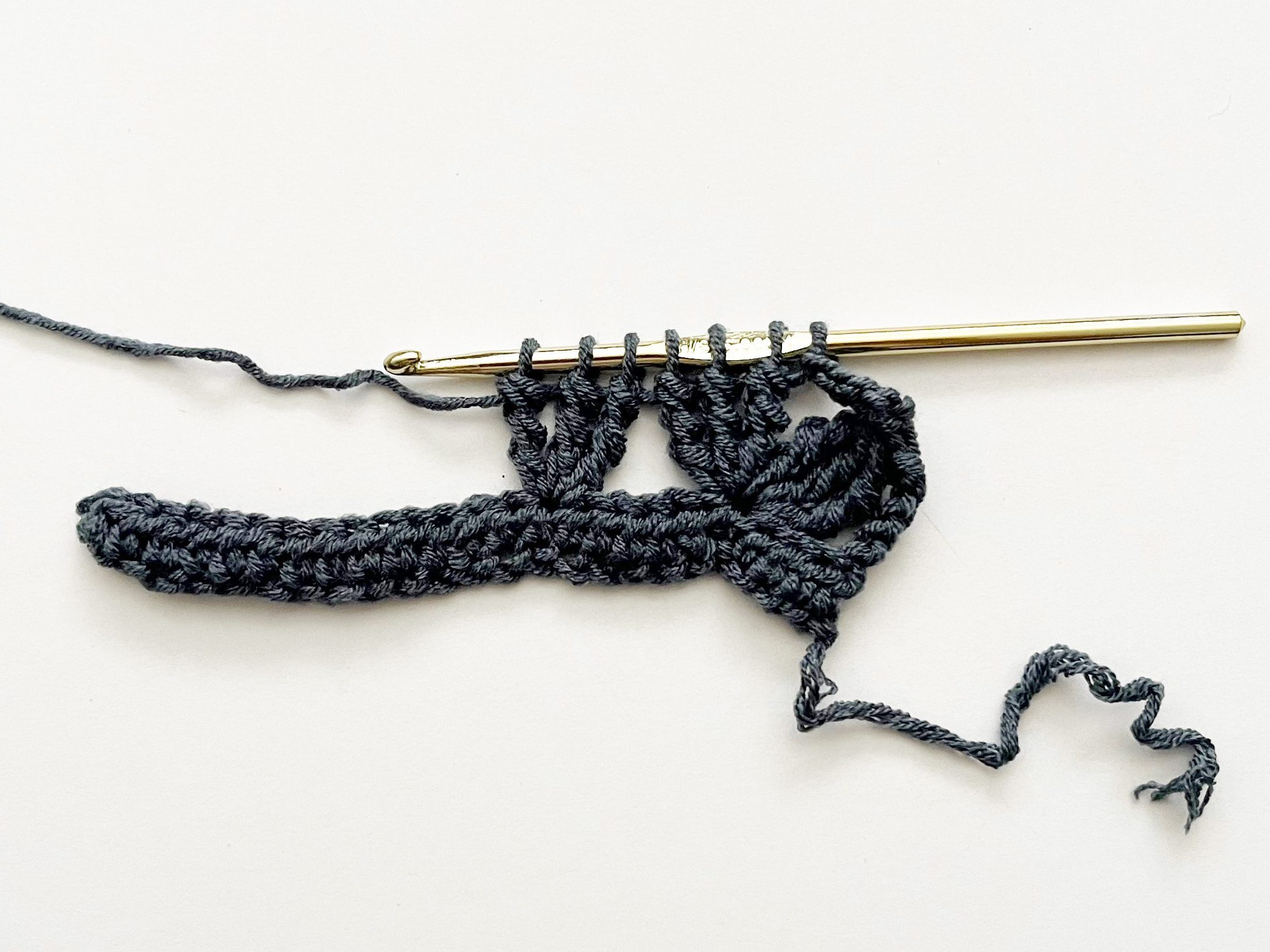denim blue yarn and gold crochet hook showing connecting two double treble crochet groups together