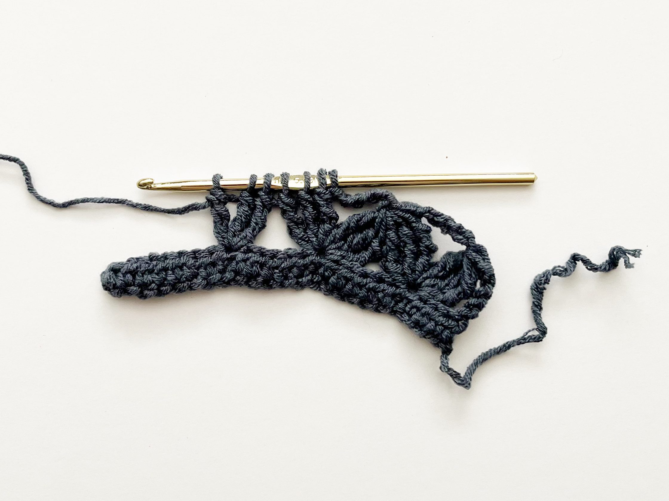 denim blue yarn and gold hook demonstrating zig zag stitch repeats