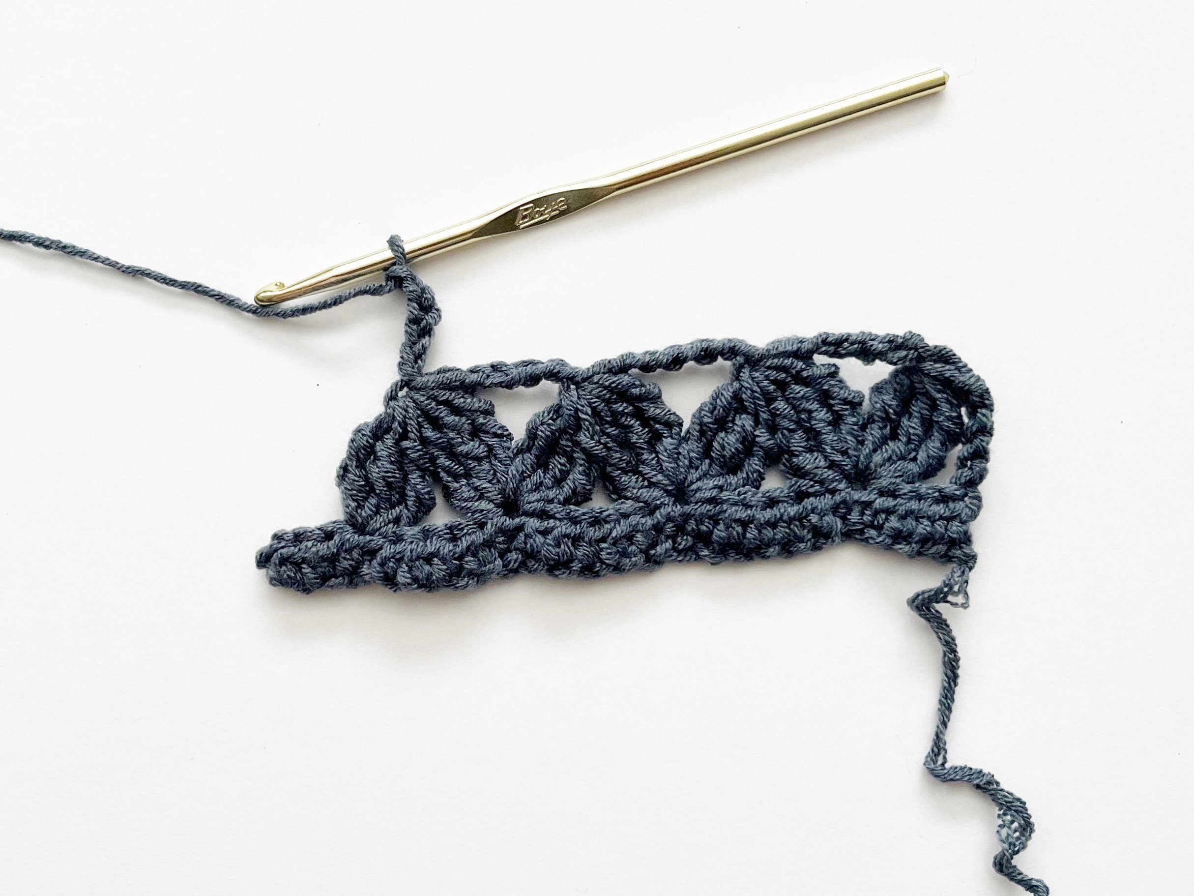 denim blue yarn and gold hook demonstrating zig zag stitch repeats