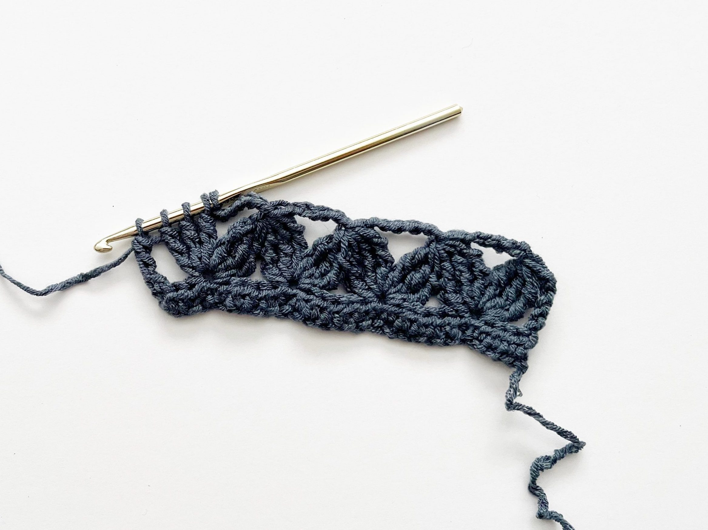 denim blue yarn and gold crochet hook showing double treble crochet stitch