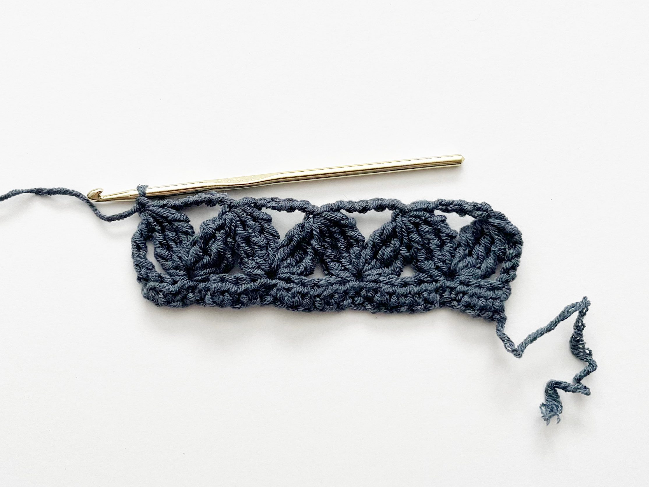 denim blue yarn and gold crochet hook showcasing zig zag crochet stitch