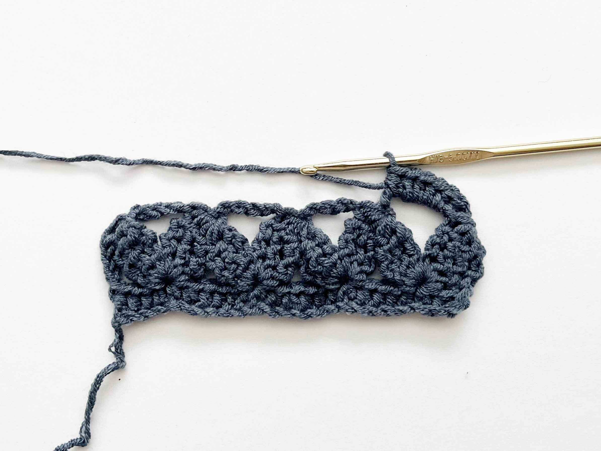 blue yarn and gold crochet hook showing placement of half double crochet stitches
