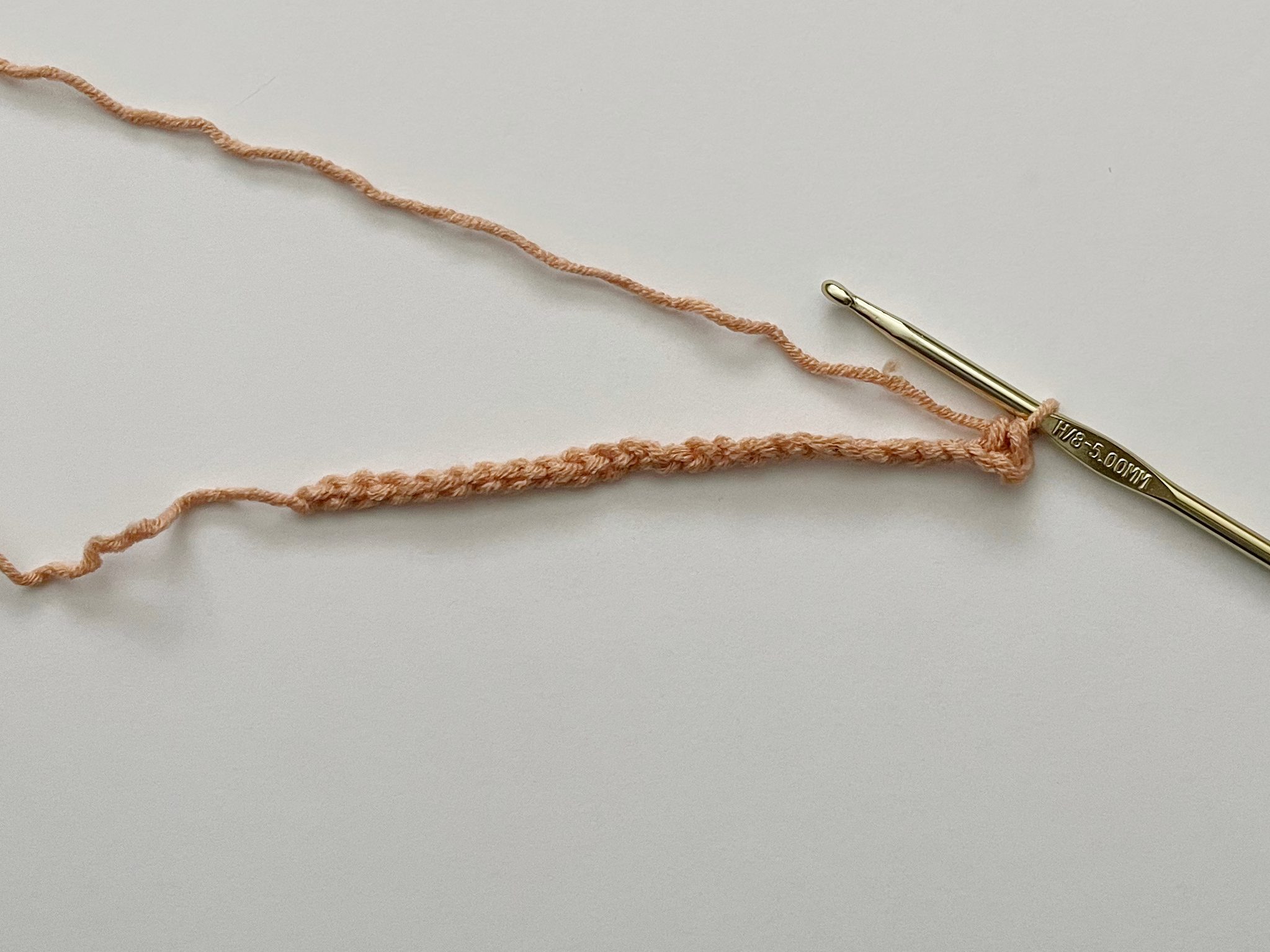 peach yarn showing single crochet stitch in chain with a gold hook