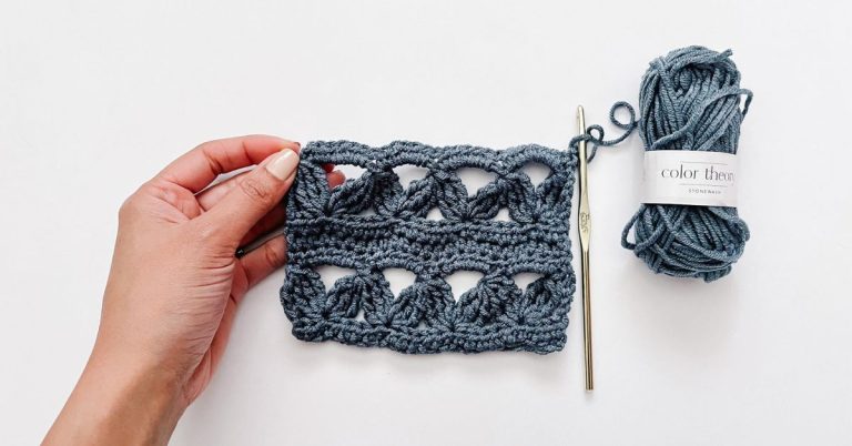 hand hold denim blue crochet swatch next to gold hook and blue mini skein of yarn on white background