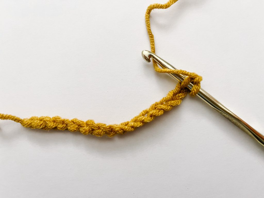 yellow yarn showing yarn over on gold crochet hook