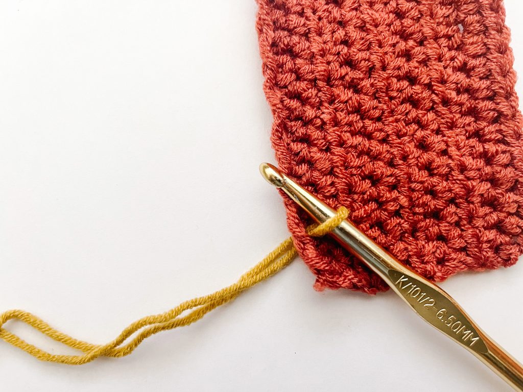 gold crochet hook pulling up a loop in yellow yarn through red crochet fabric