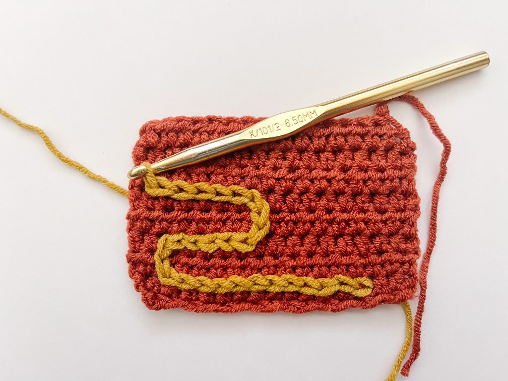 series of yellow surface slip stitches on red crochet fabric with gold crochet hook