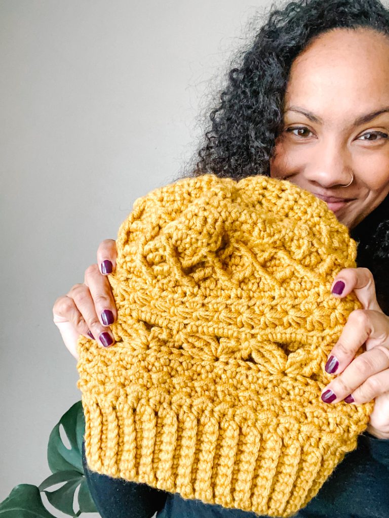 woman in background holding up mustard yellow crochet beanie