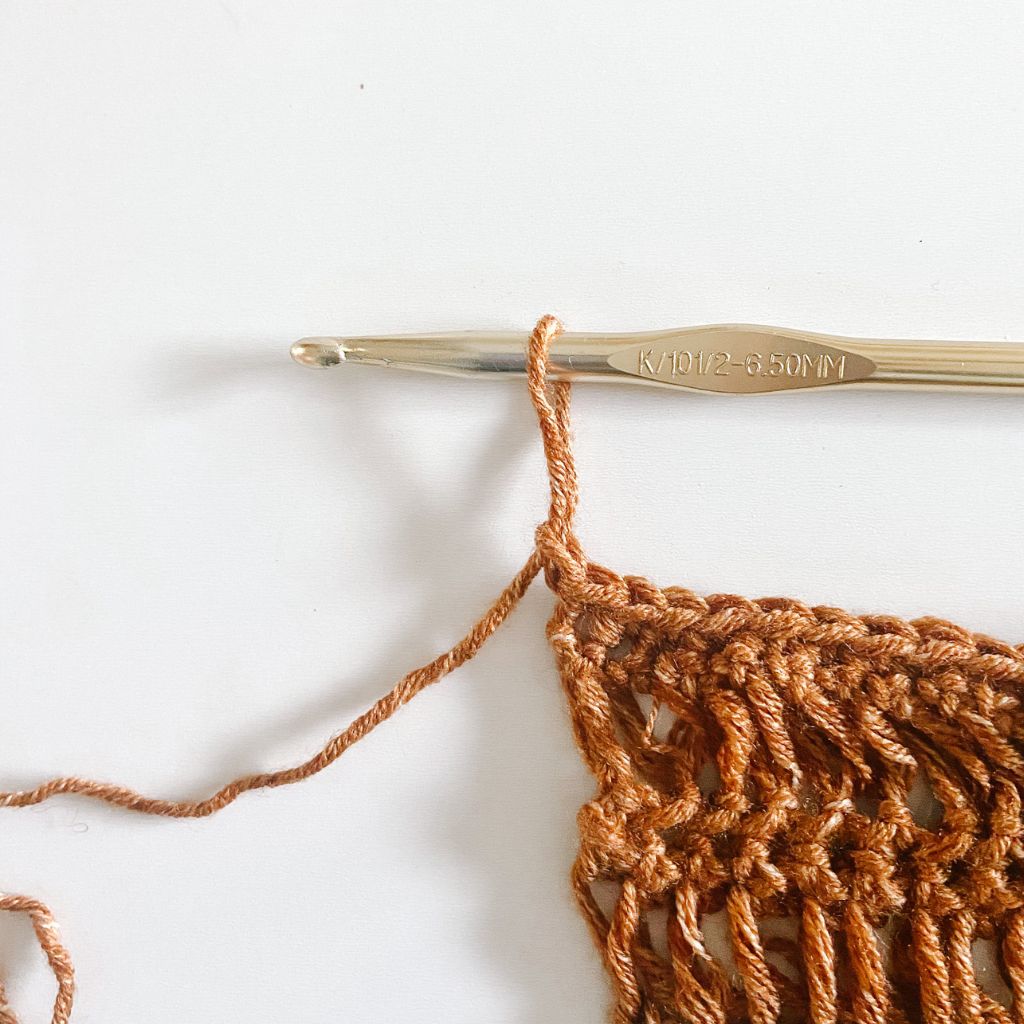 gold hook pulling up a long loop on brown crochet fabric
