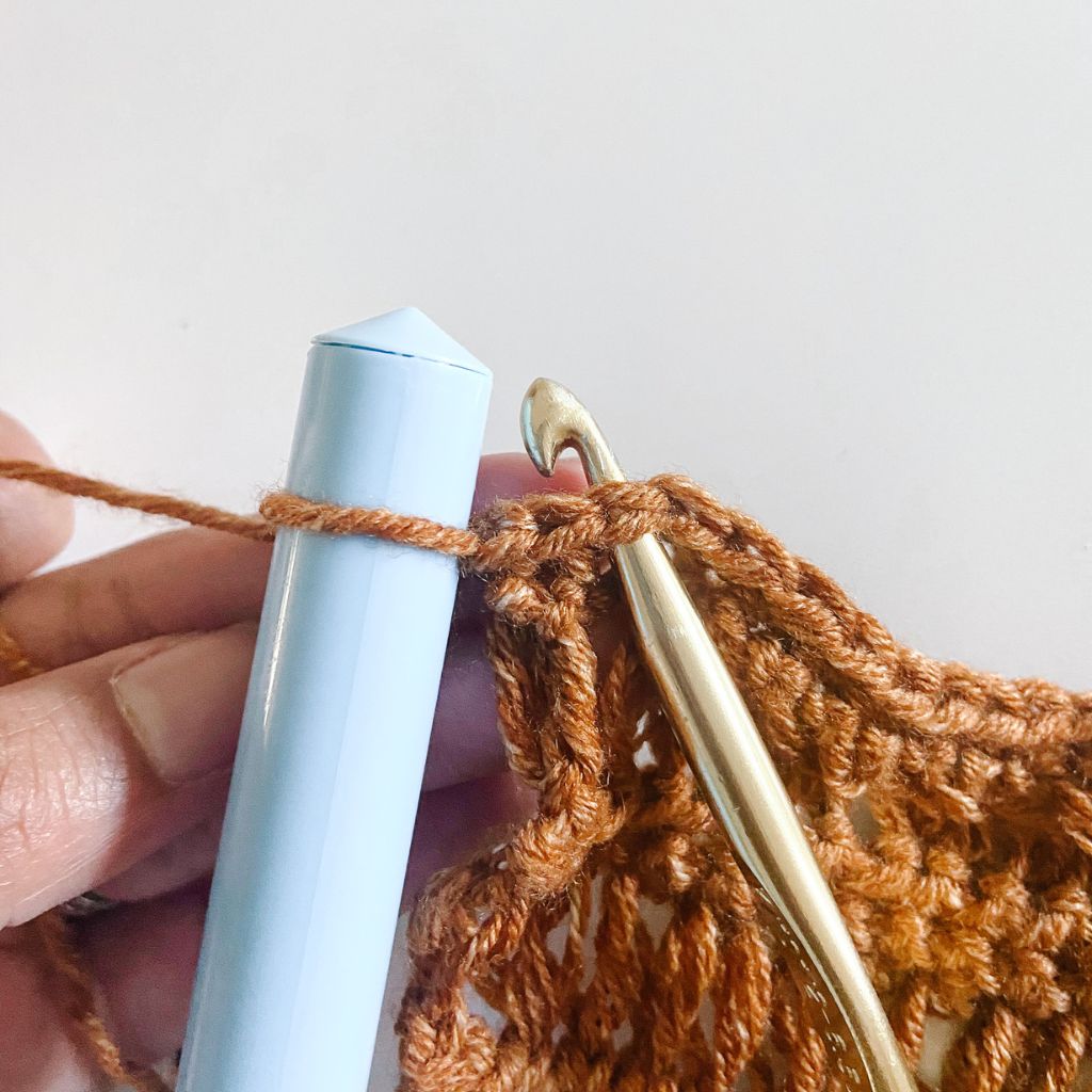 gold crochet hook in brown yarn with light blue dowel