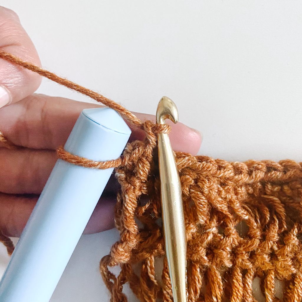 gold crochet hook in brown yarn with light blue dowel