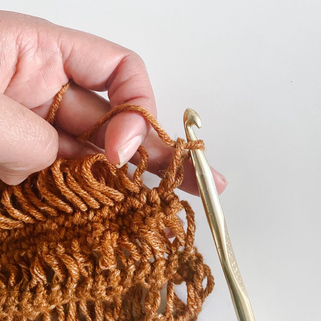 gold crochet hook pulling up loop in a crochet drop stitch